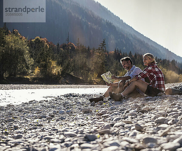 Happy friends sitting on pebbles near river