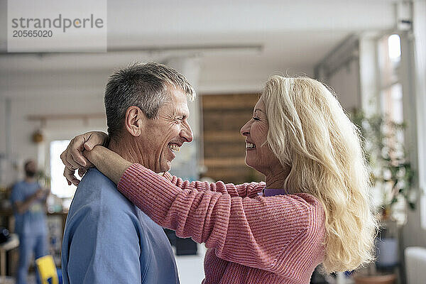 Cheerful retired loving senior woman with arms around man at home