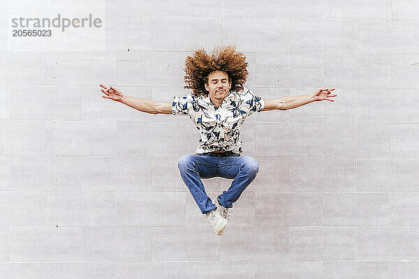 Man with arms outstretched jumping in front of wall