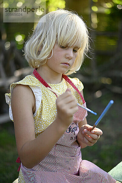 Blond hair girl painting on stick with brush