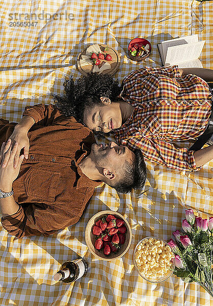 Multiracial couple lying face to face on picnic blanket