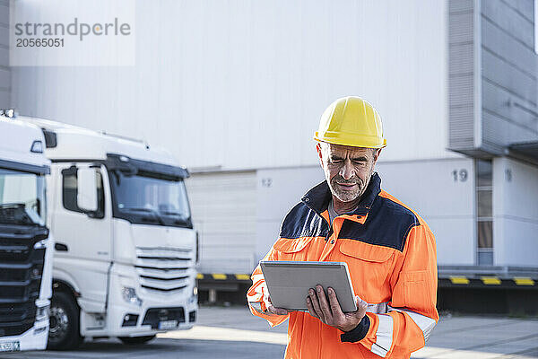 Confident mature foreperson wearing protective workwear using tablet PC at warehouse