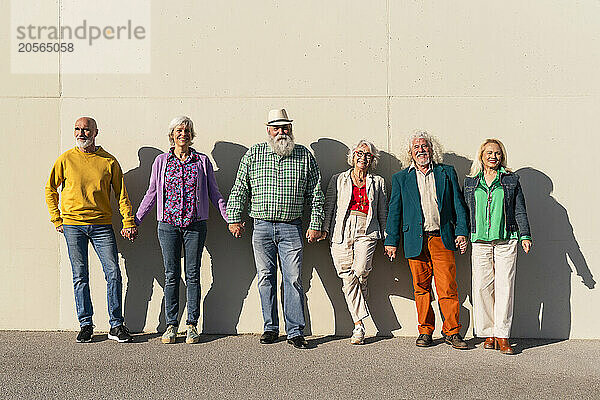 Retired women and men holding hands standing in front of wall on sunny day