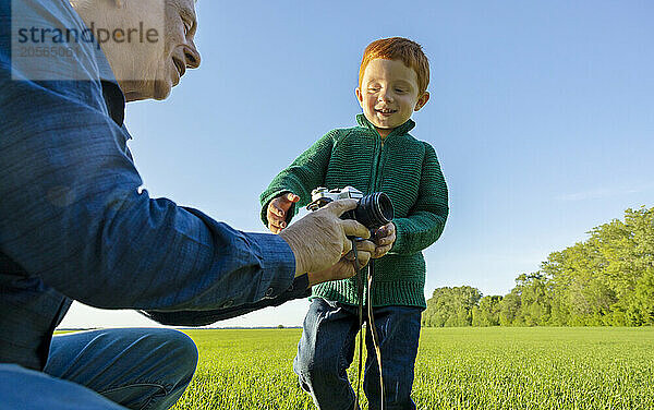 Grandfather gives old camera to his grandson in field