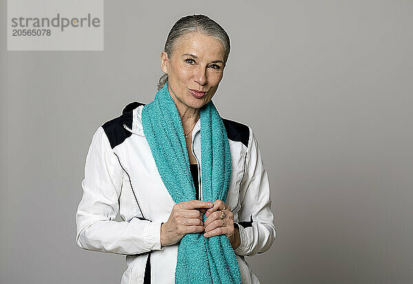 Smiling senior woman with turquoise towel puckering against gray background