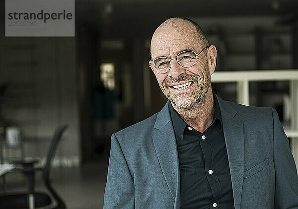 Smiling mature businessman with stubble wearing eyeglasses in office