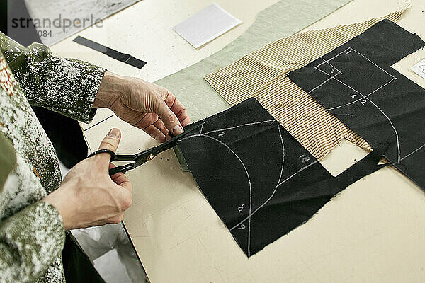 Fashion designer cutting cloth sample at workshop