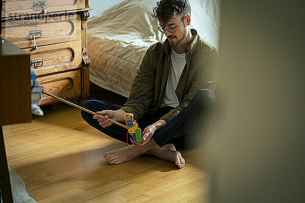 Young man sitting in bedroom playing with toy at home