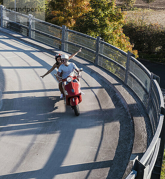 Happy young couple having fun on motor scooter on curve road