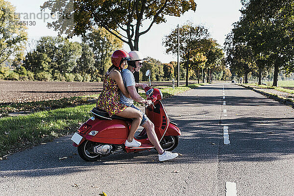 Cheerful young couple riding motor scooter at country road