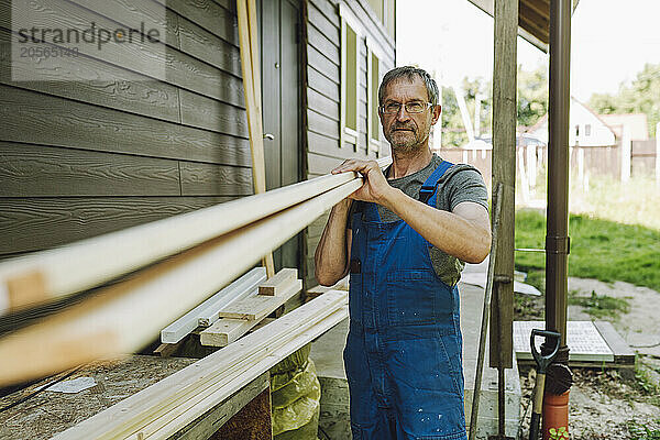 Confident mature man carrying planks at back yard