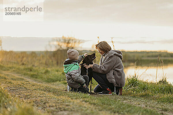 Mother and son spending leisure time with dog on footpath at sunset