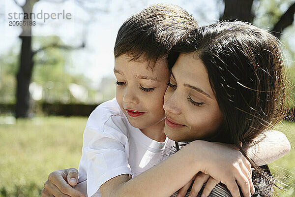 Cute boy with arm around mother embracing at park