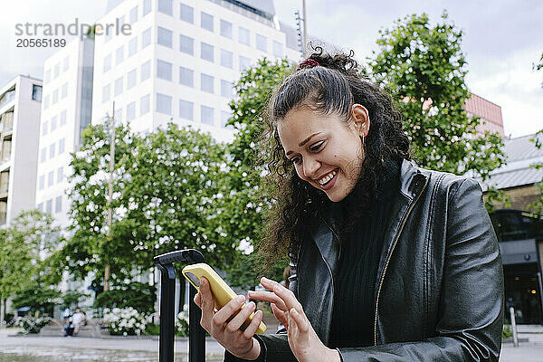 Happy beautiful young woman using mobile phone in city