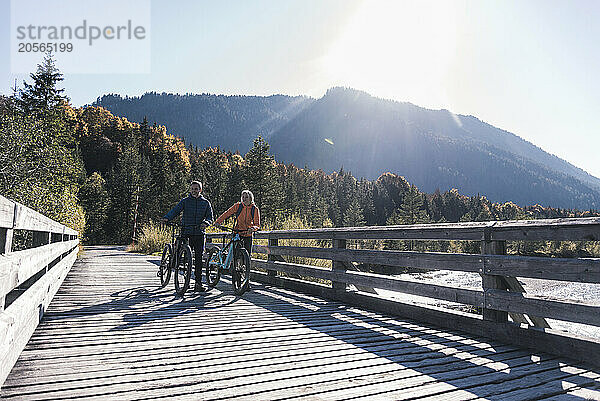 Mature couple with bicycles on boardwalk at sunny day