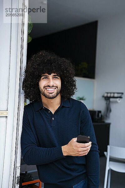 Smiling businessman with mobile phone leaning on doorway