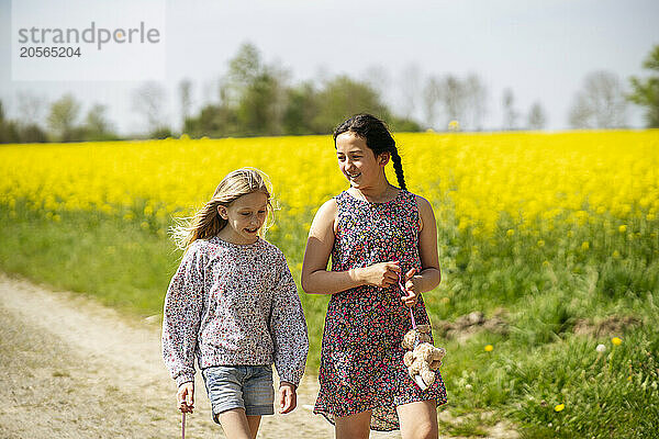 Smiling girls talking and walking together at oilseed field