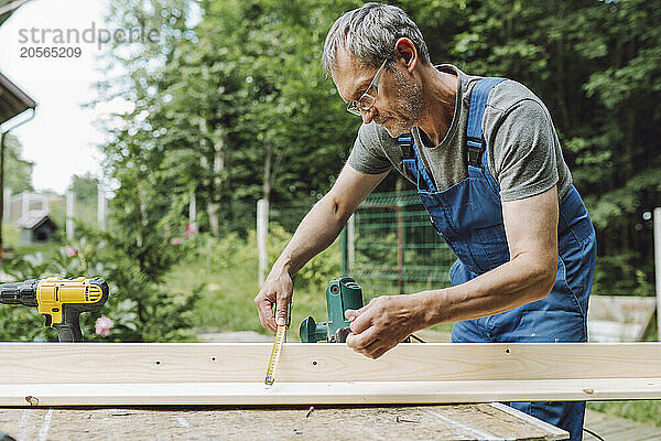 Confident man measuring plank with tape at back yard