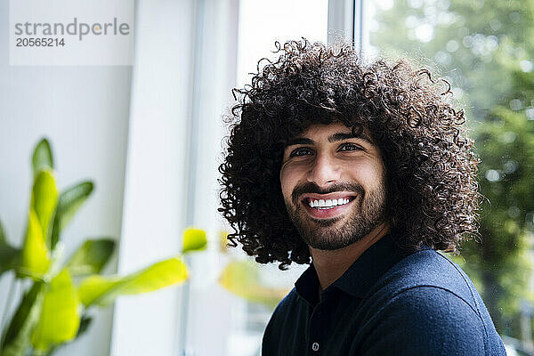 Smiling young handsome businessman with curly hair in office