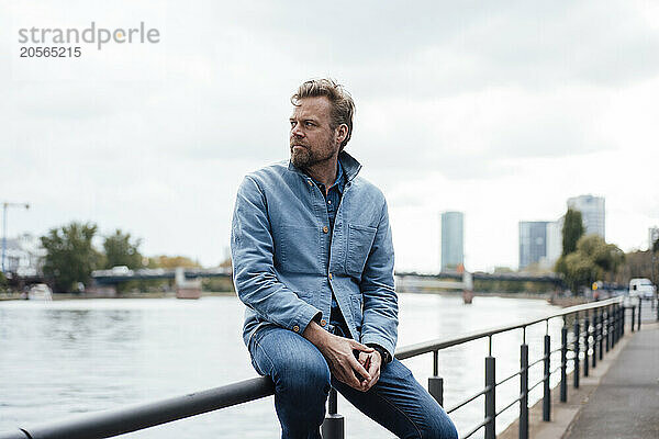 Mature man sitting on railing by river