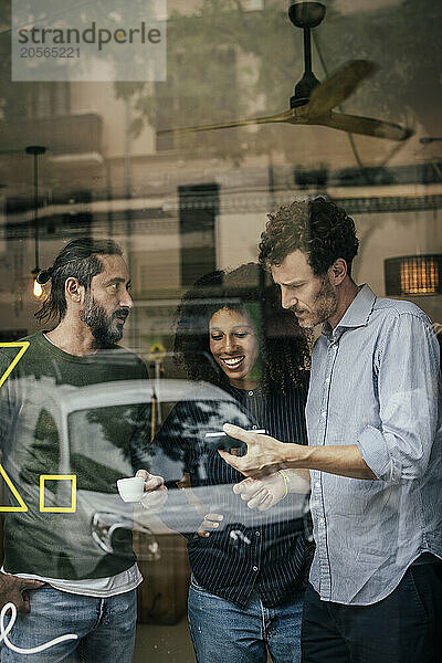 Businessman sharing smartphone with colleagues at cafe