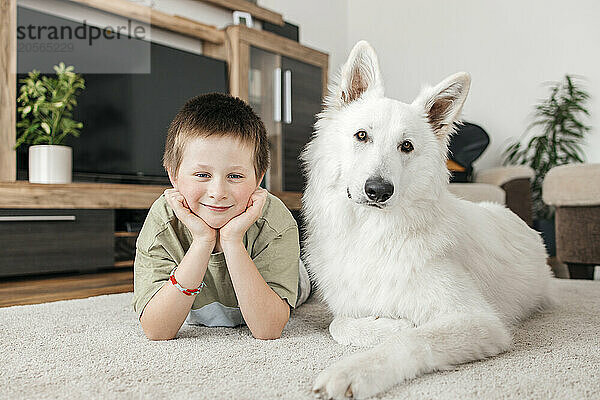 Cute boy with swiss shepherd dog lying on carpet floor at home