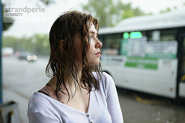 Thoughtful woman with wet hair waiting at bus stop