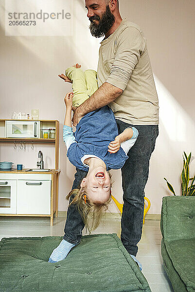 Father holding daughter upside down at home