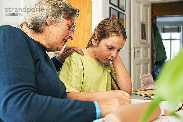 Senior woman with hand on shoulder of grandson doing homework