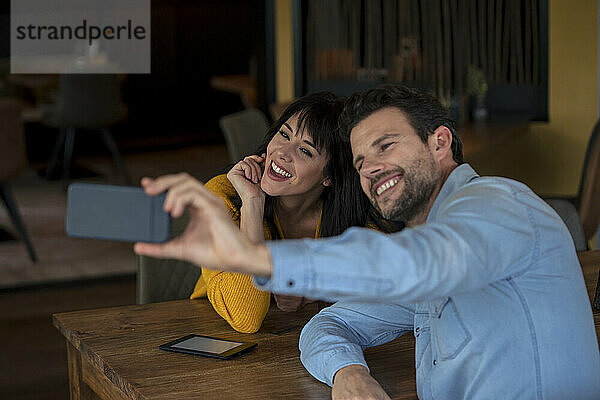 Cheerful businessman taking selfie with businesswoman through smart phone in cafe