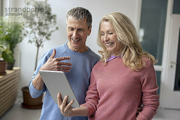 Smiling senior couple sharing tablet PC at home