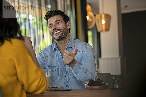 Happy businessman talking to businesswoman sitting at table in cafe