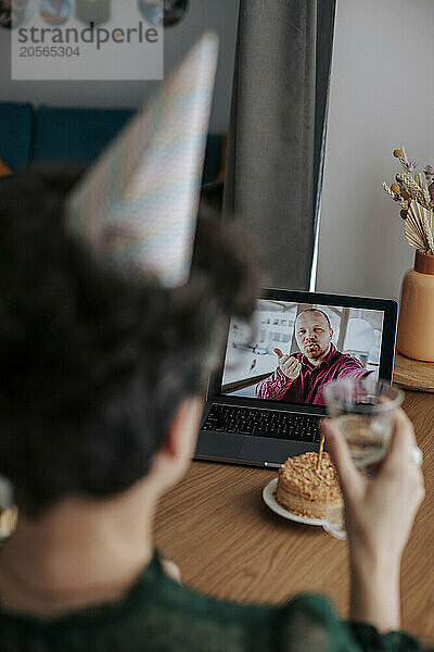 Man blowing kiss through video call and woman toasting wine at home