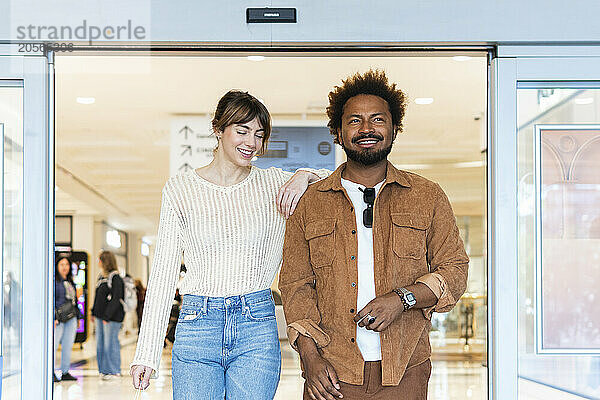 Smiling multicultural couple leaving shopping mall