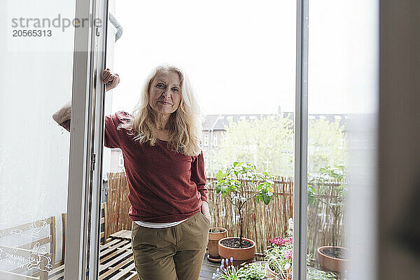 Smiling retired senior woman leaning on balcony doorway