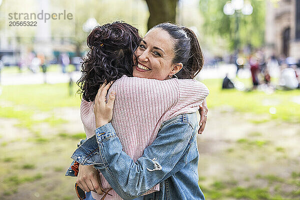 Smiling woman hugging female friend standing at park