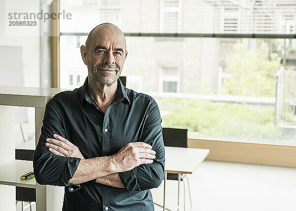 Confident mature businessman with arms crossed standing in office