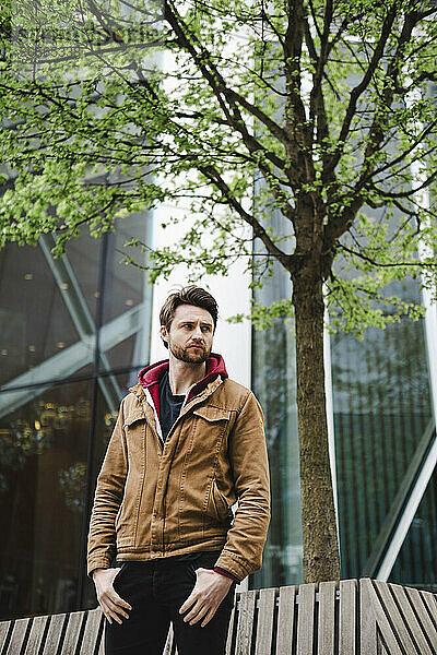 Man with hands in pockets posing in front of tree