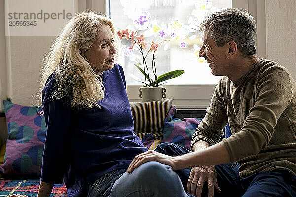 Smiling retired senior couple sitting on alcove window seat at home