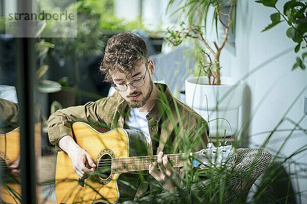 Young man playing music on guitar practicing at home