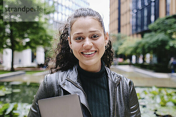 Smiling young businesswoman with laptop in city