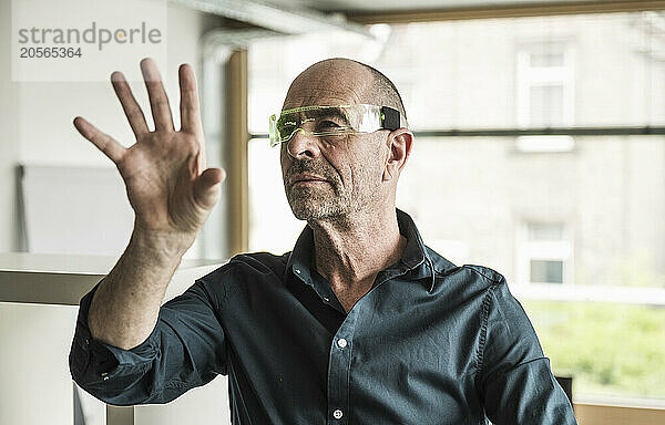 Confident businessman wearing smart glasses gesturing in office