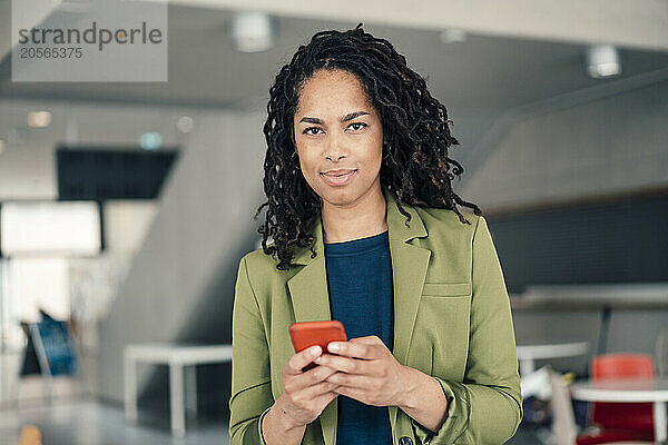 Confident young beautiful businesswoman using smart phone standing at office