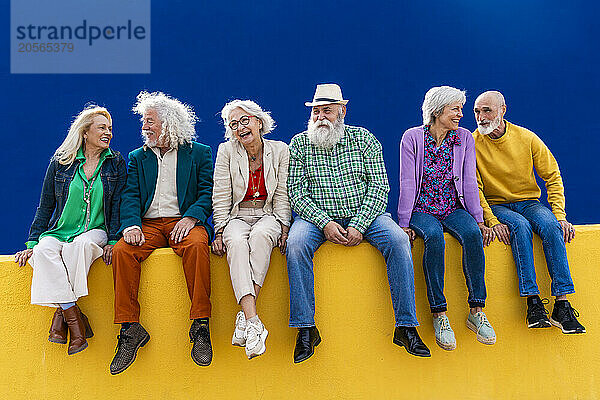 Happy senior friends sitting on wall