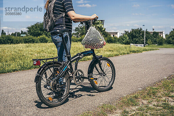 Mature woman carrying groceries in reusable bag and walking with bicycle on road