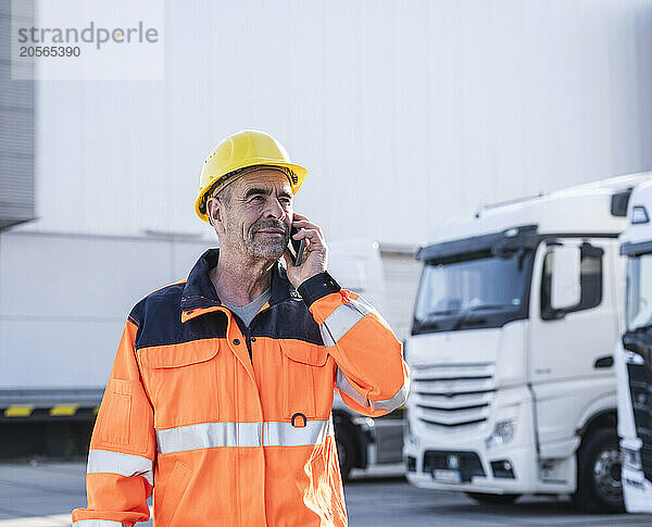 Confident dock worker wearing protective workwear talking on mobile phone at warehouse