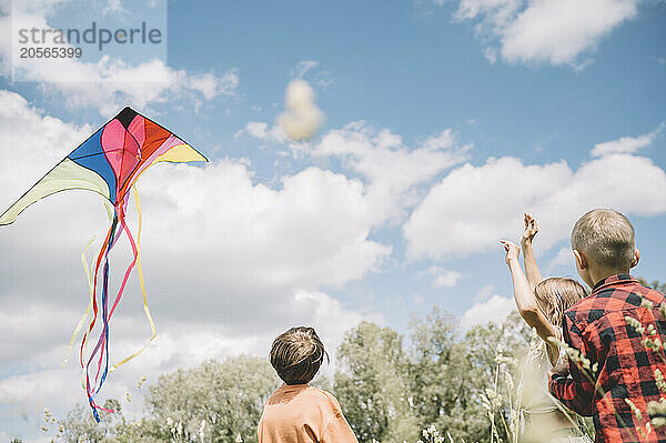 Girl flying kite with brothers on sunny day