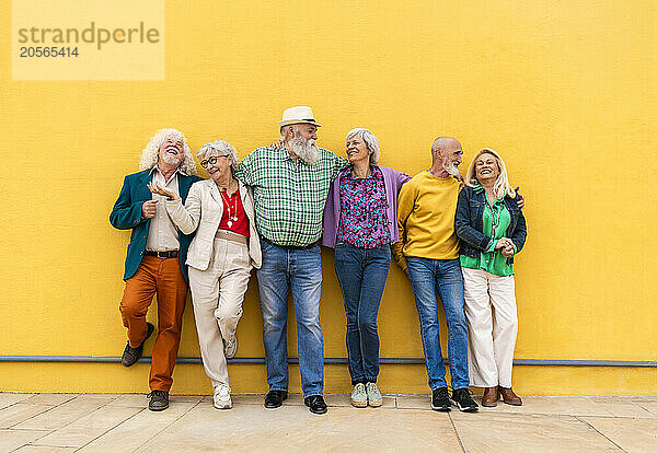 Happy senior friends talking in front of yellow wall