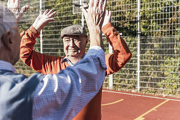 Active senior friends playing and giving high five at basketball court