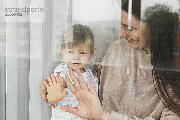 Mother with baby girl looking out through glass window